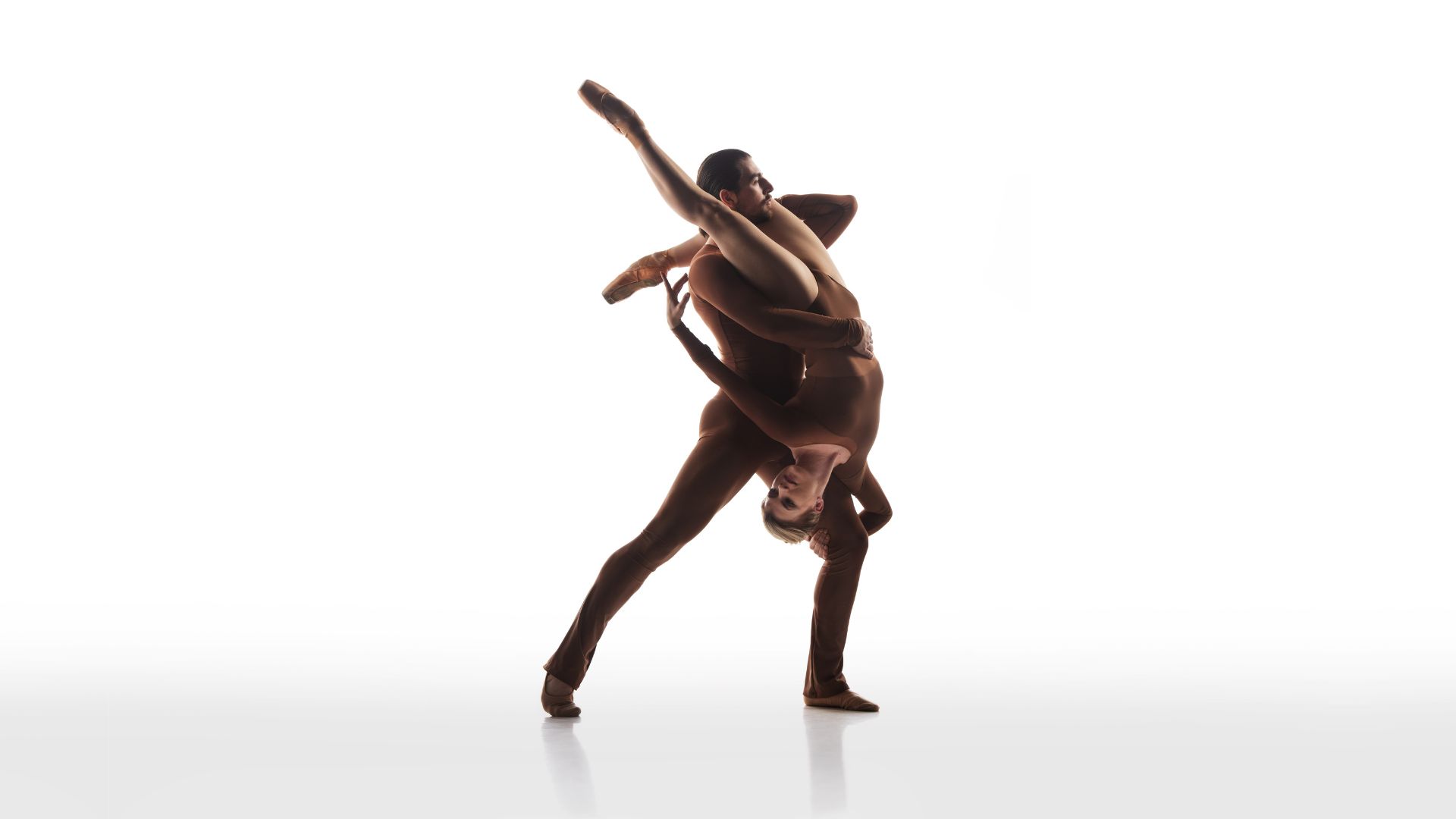 Two dancers in skin-toned outfits. One holding the other upside down.